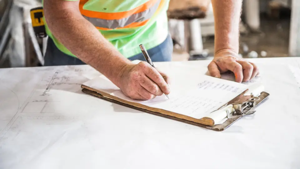 Worker in hi-vis filling in a paper checklist on a clipboard